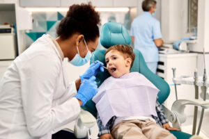 Black female dentist examining small boy's teeth during dental procedure at dentist's office. Focus is on boy.