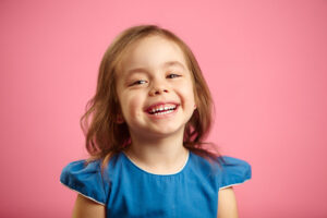 Cheerful little girl with charming smile and hearty laugh on pink isolated background, expresses heartfelt emotions of joy, is in a good mood, portrait of beautiful kid.