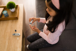 Top view of a sick kid with diabetes using a digital monitor to test her blood sugar levels at home