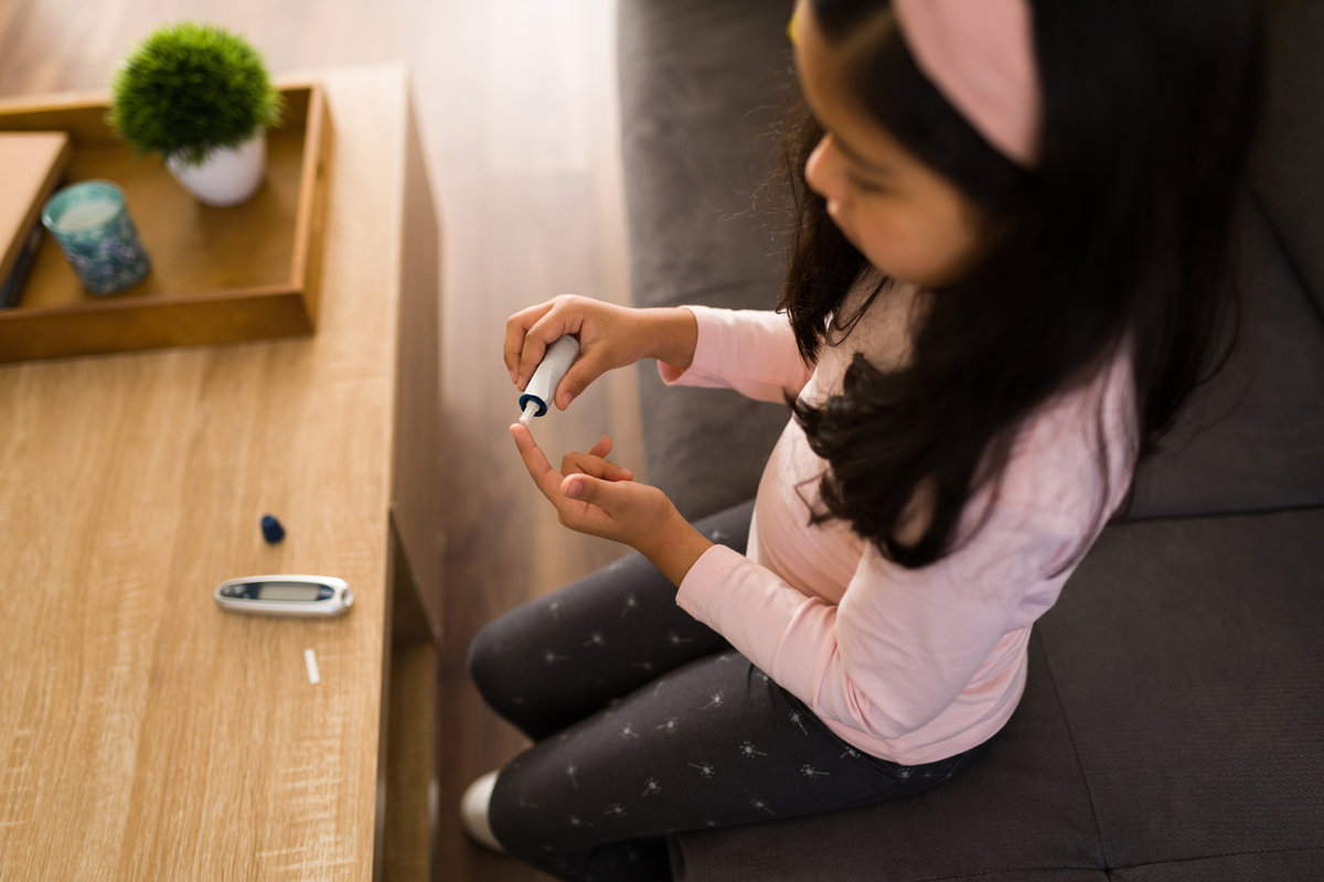 Top view of a sick kid with diabetes using a digital monitor to test her blood sugar levels at home