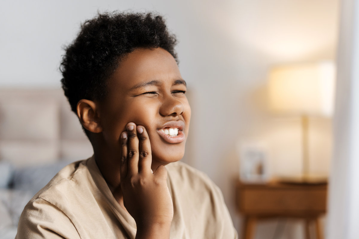 Portrait of unhealthy African American little boy touching cheek, feeling severe toothache at home. Healthy care, dental concept